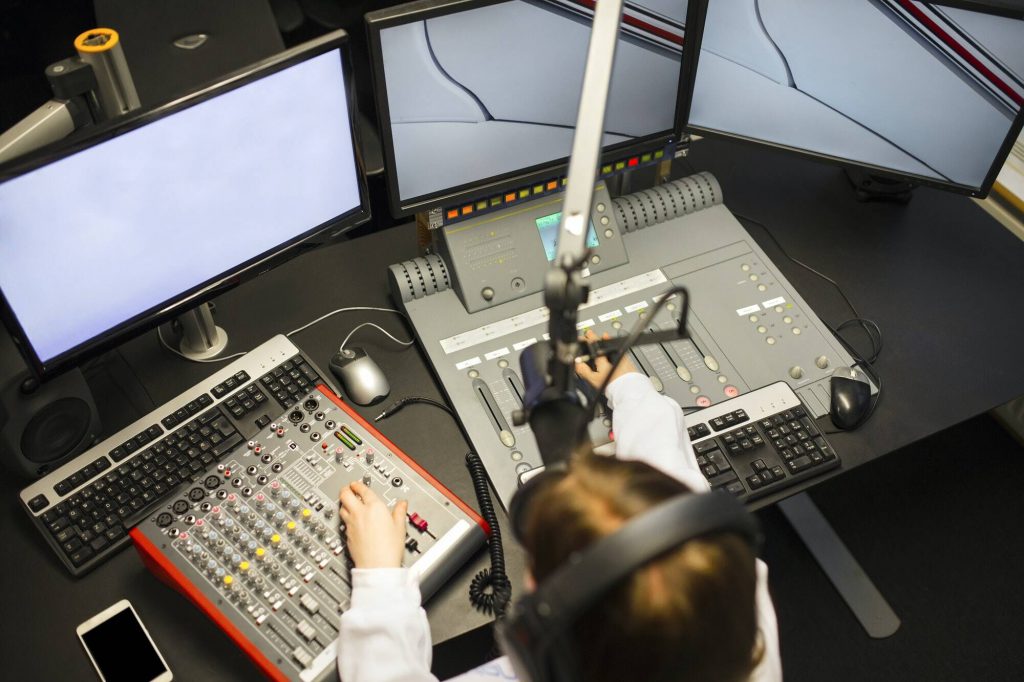 Female Jockey Using Music Mixers And Screens In Radio Studio